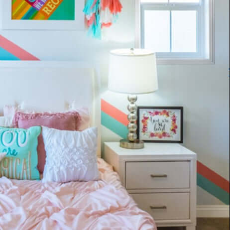 Cozy bedroom with pink bedding, decorative pillows, modern lamp, and colorful wall art.