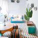 Stylish living room featuring a blue couch, wooden table, and decorative plants with colorful patterned flooring.