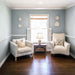 Cozy living room featuring light blue walls, two armchairs, a small table, and decorative wall elements.