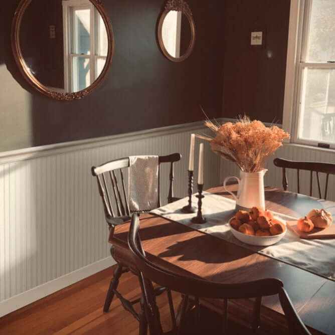 Cozy dining room featuring a wooden table, black chairs, decorative mirrors, and a centerpiece of dried flowers and fruit.